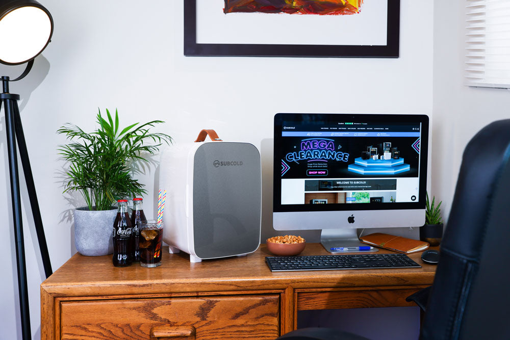 Portable mini fridge next to a computer setup with grey front and tan handle
