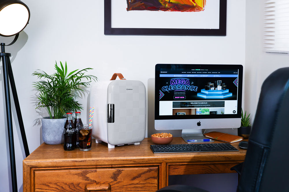 Portable mini fridge in light grey on desk with compact design and top carry handle