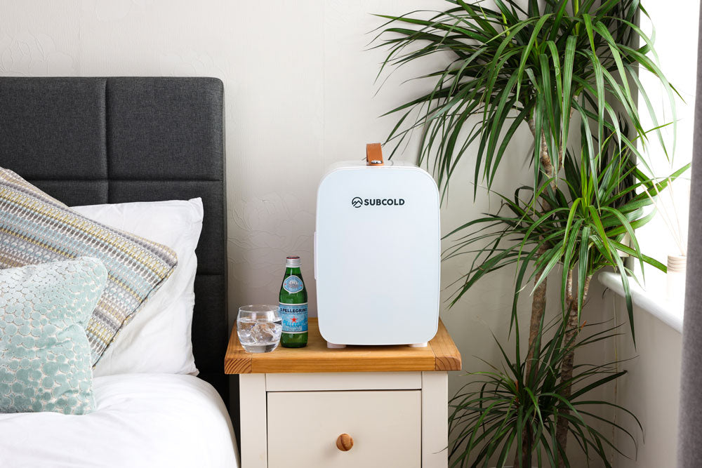White portable mini fridge on a side table in a bedroom setting