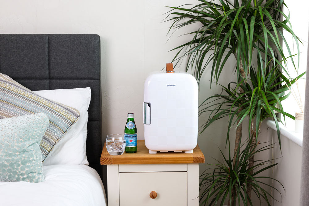 White portable mini fridge with silver door handle and brown carry strap on a side table