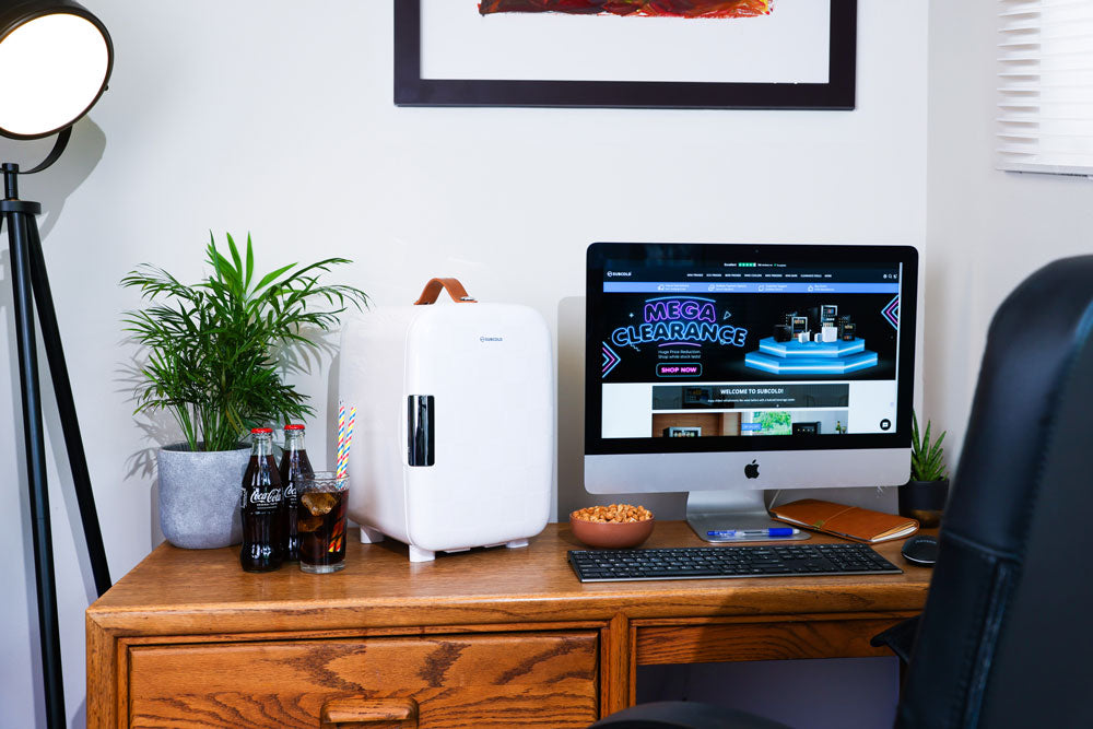 White portable mini fridge with brown carry strap, standing on a wooden cabinet