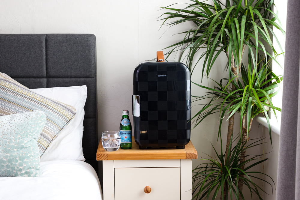 Black checker portable mini fridge on a bedside table beside a plant