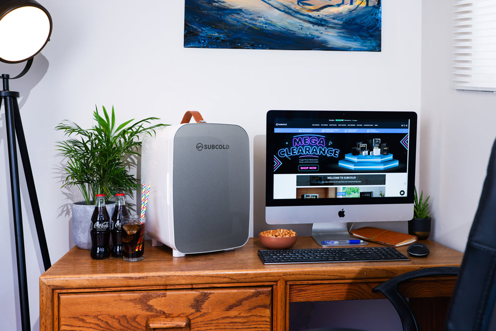 Portable mini fridge on desk next to computer monitor in a home workspace