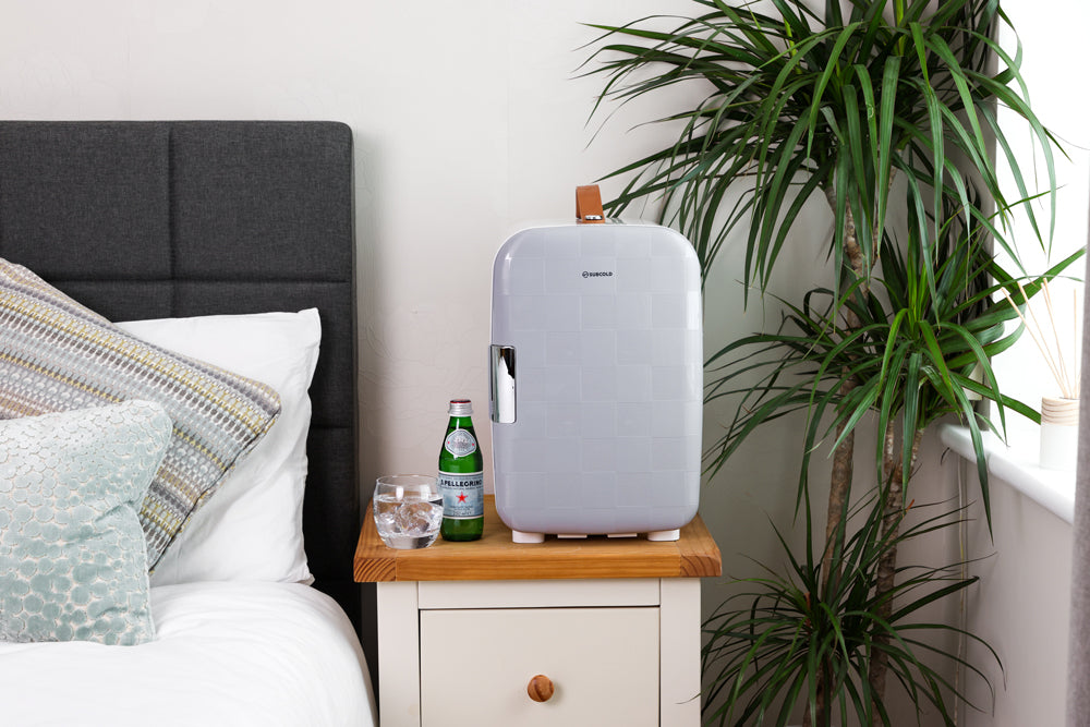 White portable mini fridge with front door and side handle, placed on a small cabinet.