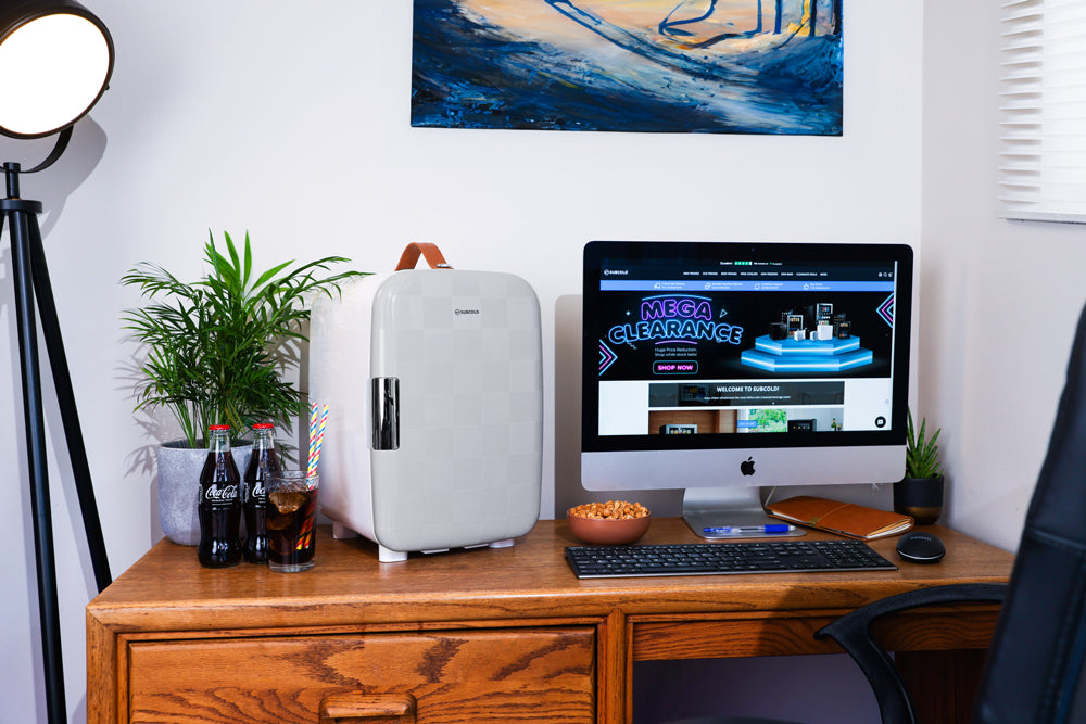 White portable mini fridge on a wooden desk in a home office setting.