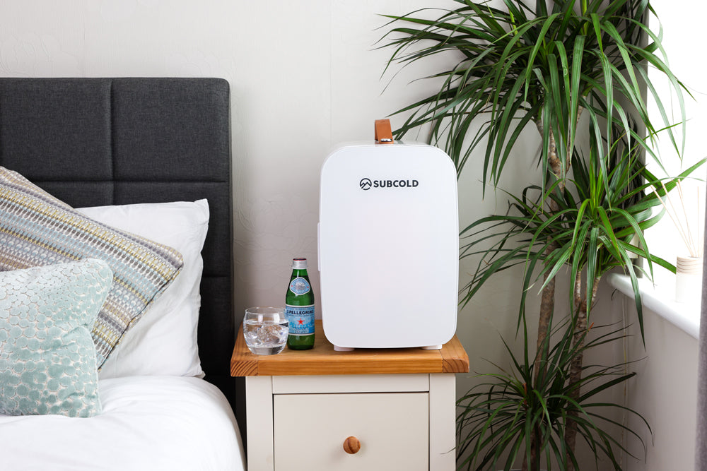 White portable mini fridge on a bedside table with carry handle