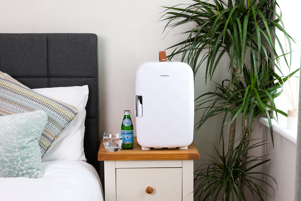 White compact mini fridge on a bedside table with side view and carry handle.