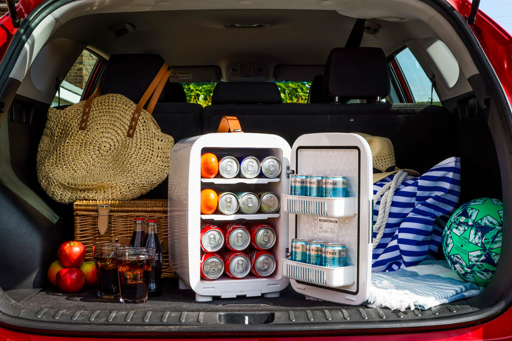 White portable mini fridge loaded with drinks and food inside an open vehicle trunk.