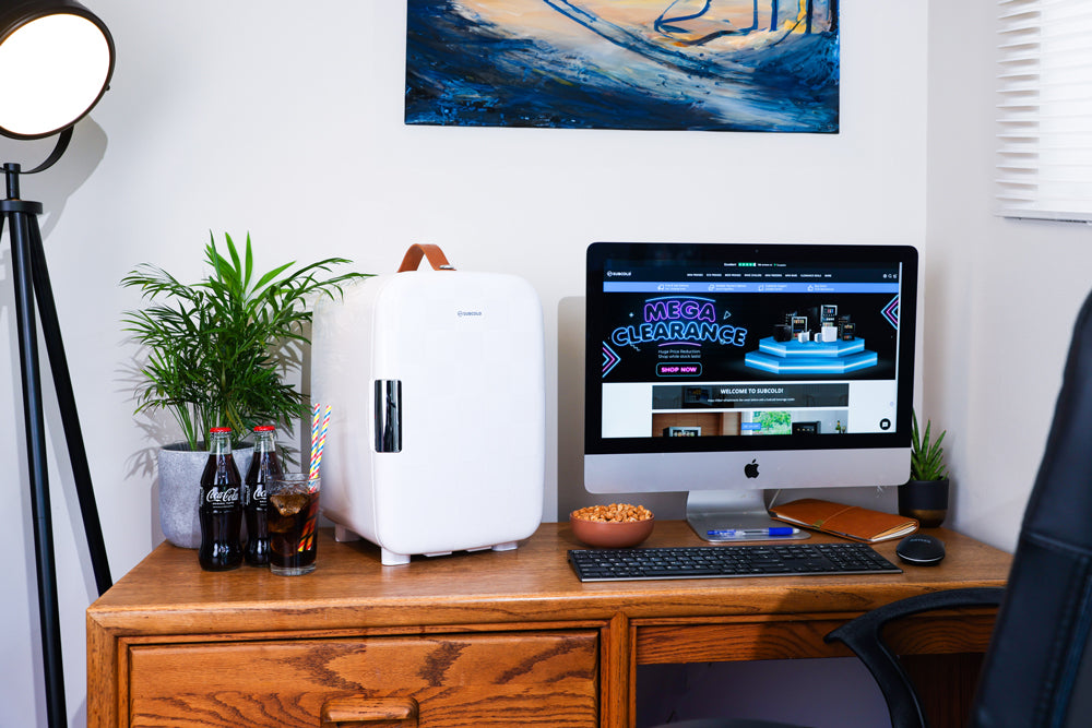 White mini fridge on a desk with side view, chrome handle, and leather carry strap.