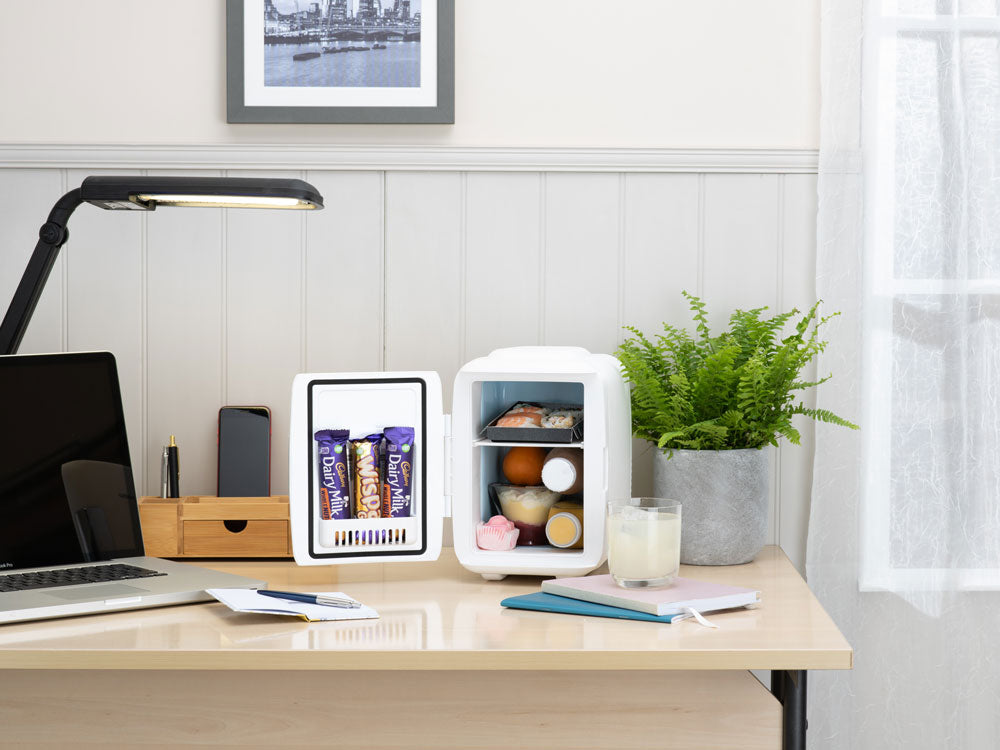 Portable mini fridge on a desk with open door and snacks inside