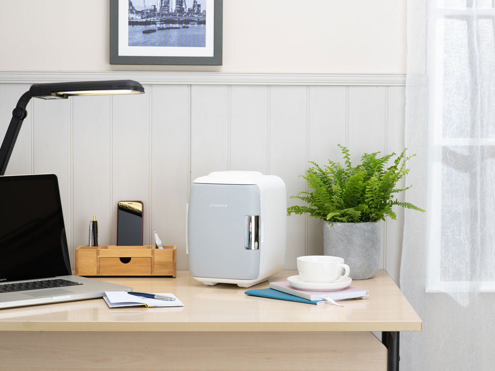 White mini fridge on a desk in a home office setting, closed door