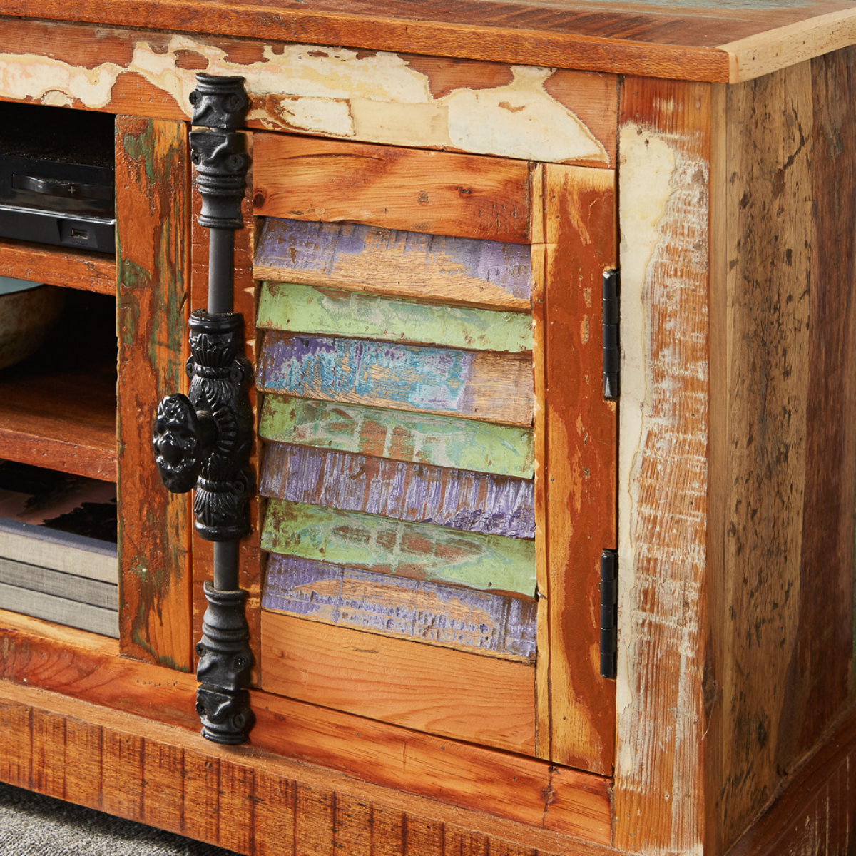 Close-up of distressed cabinet door with black metal handle and colorful wood slat interior