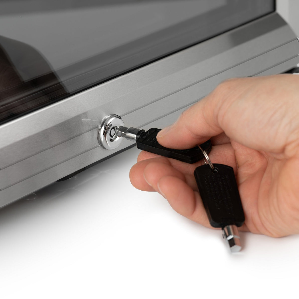 Hand with key unlocking a black drinks fridge door lock