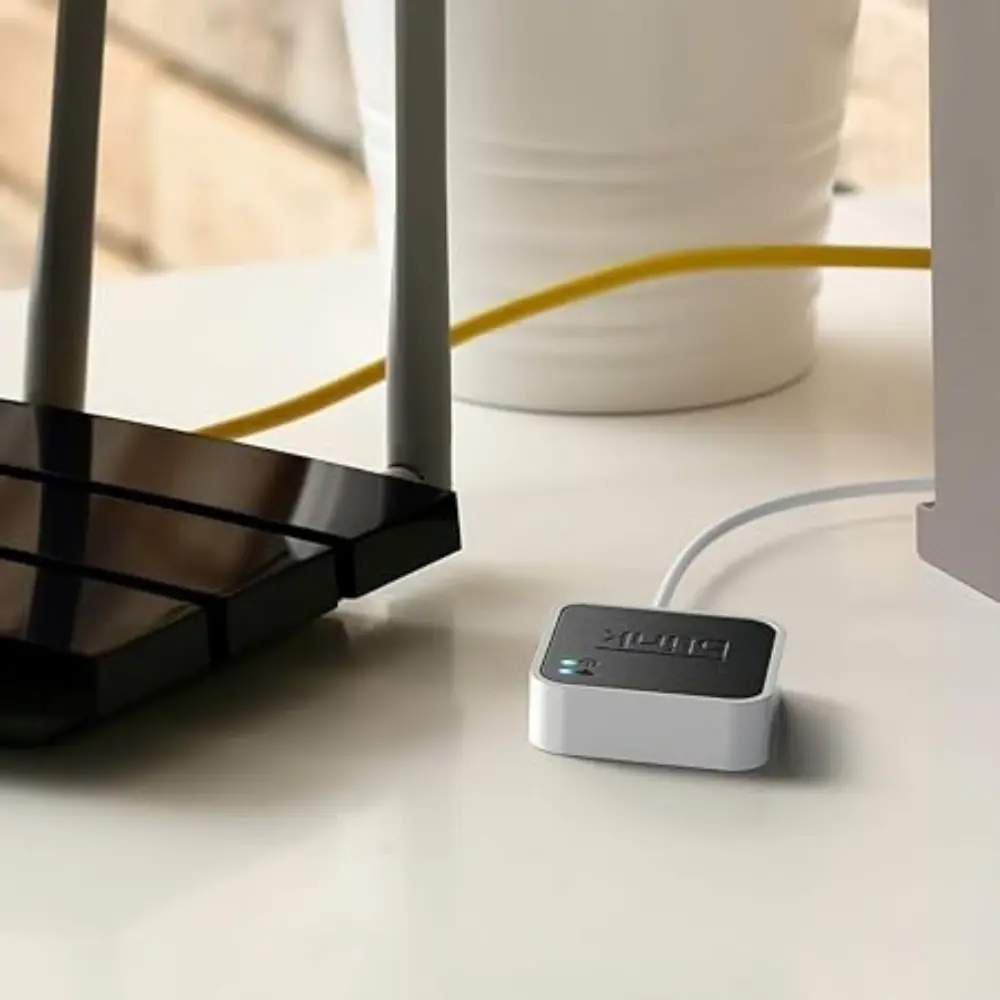 White Blink sync module with green LED lit on desk near connected cables.