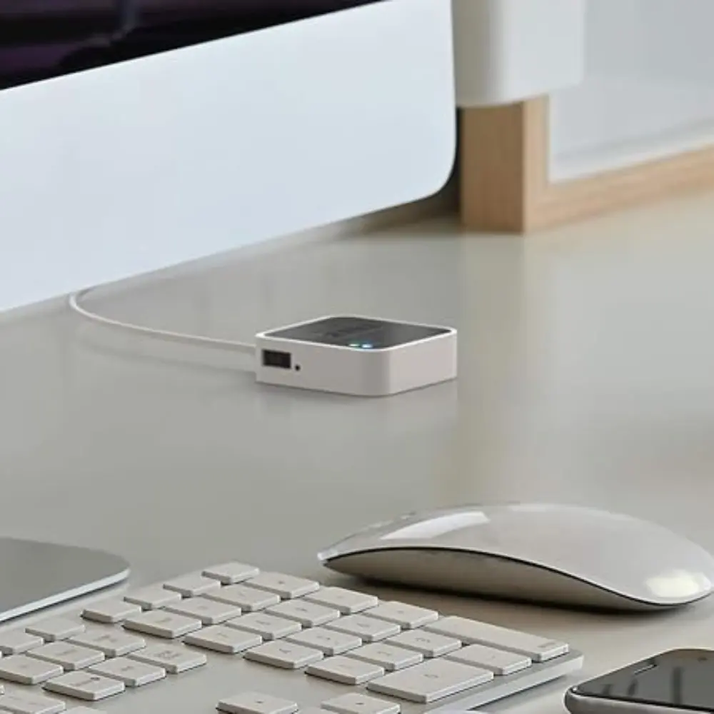 Compact white Blink sync module on desk near keyboard and mouse, green LED on.
