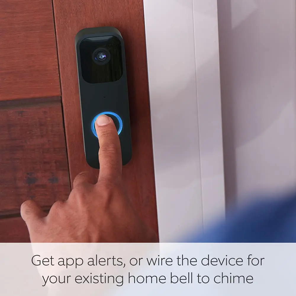 Black video doorbell on a door with a finger pressing the blue button ring