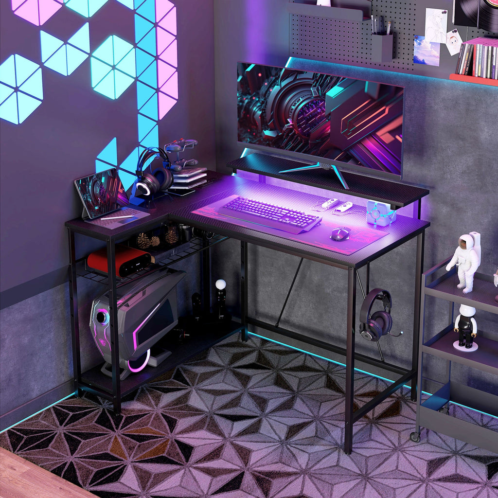 Black L-shaped desk with RGB LED strip, keyboard, and monitor setup with shelves.