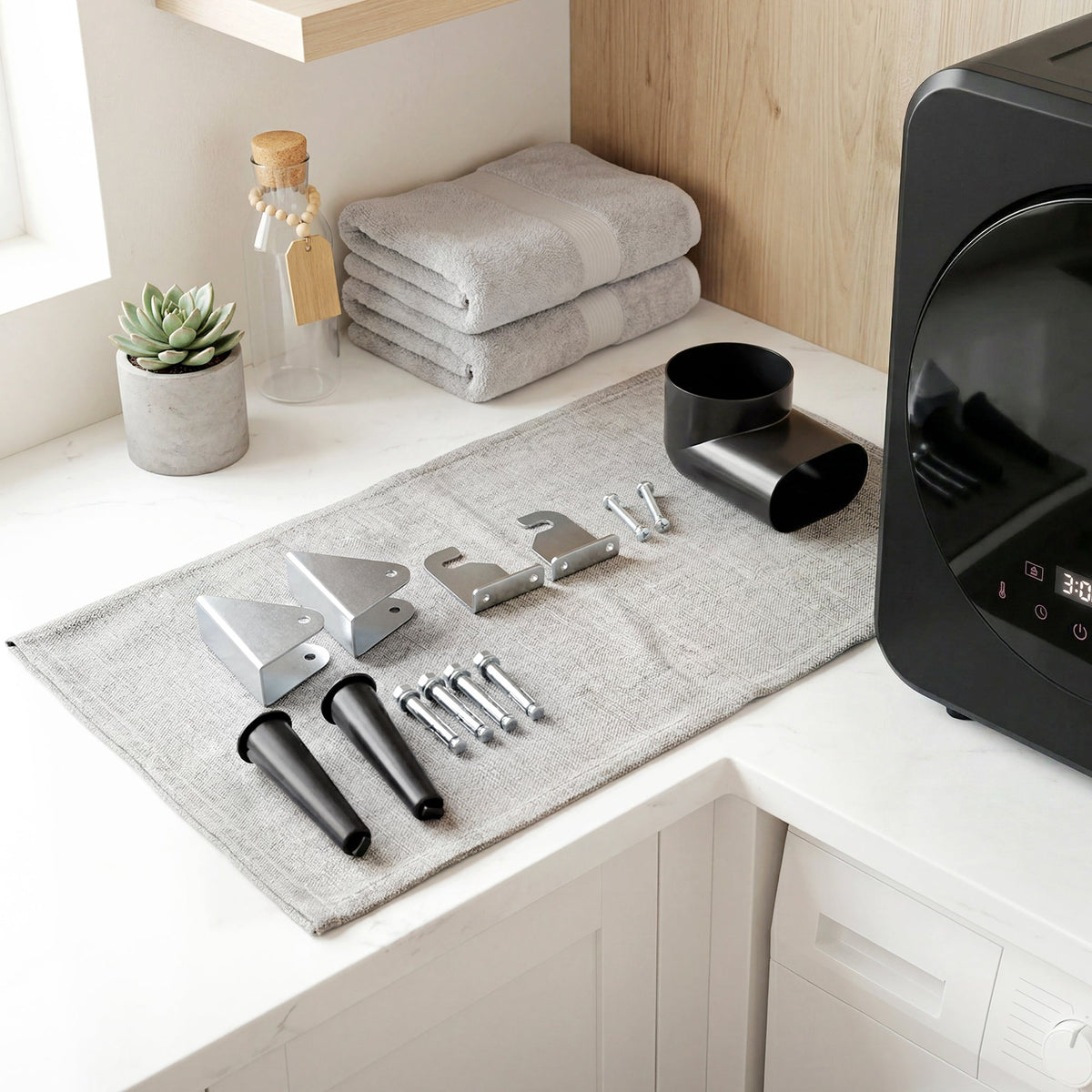 Black tumble dryer with included installation tools and vent parts on a mat