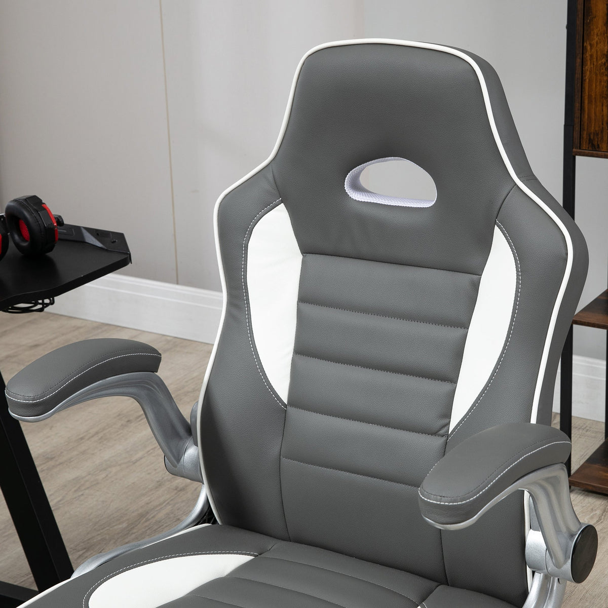 Grey gaming chair close-up of padded back and seat with stitching and curved flip-up armrest