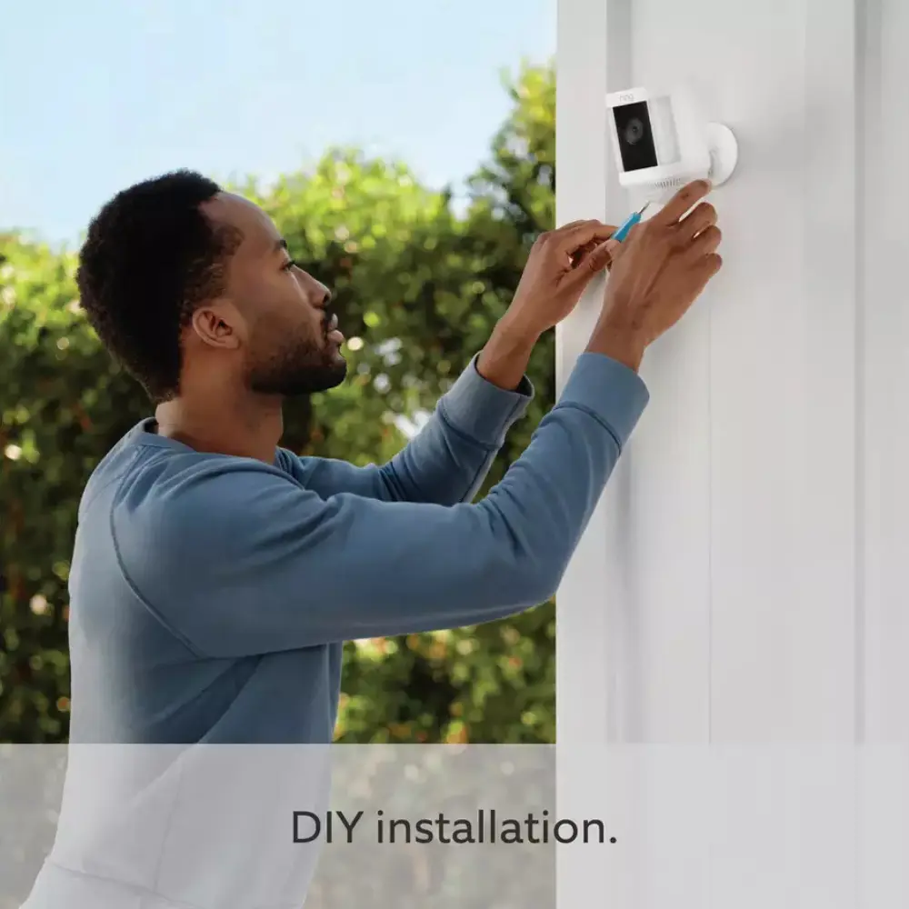 Person mounting a Ring spotlight security camera on a white exterior wall