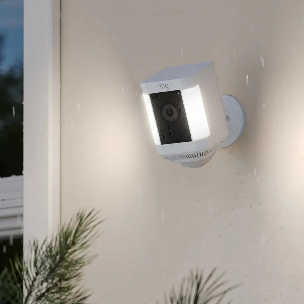 Ring Spotlight Cam Plus plug-in outdoor security camera in white under rain on wall