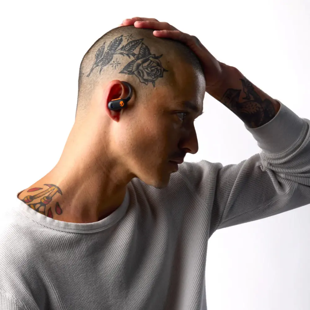 Black orange in-ear earbuds worn by person with tattoos