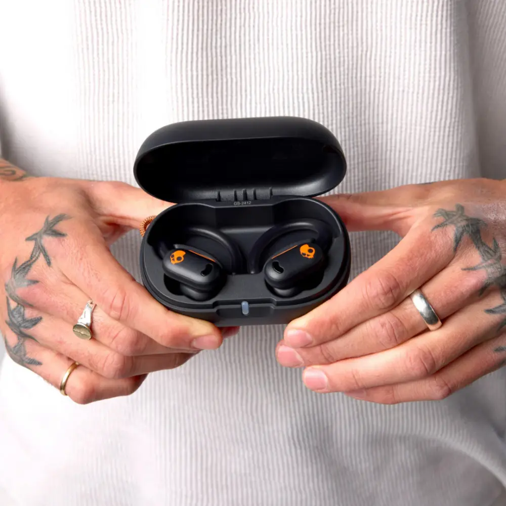 Black earbuds closed inside open charging case held by hands