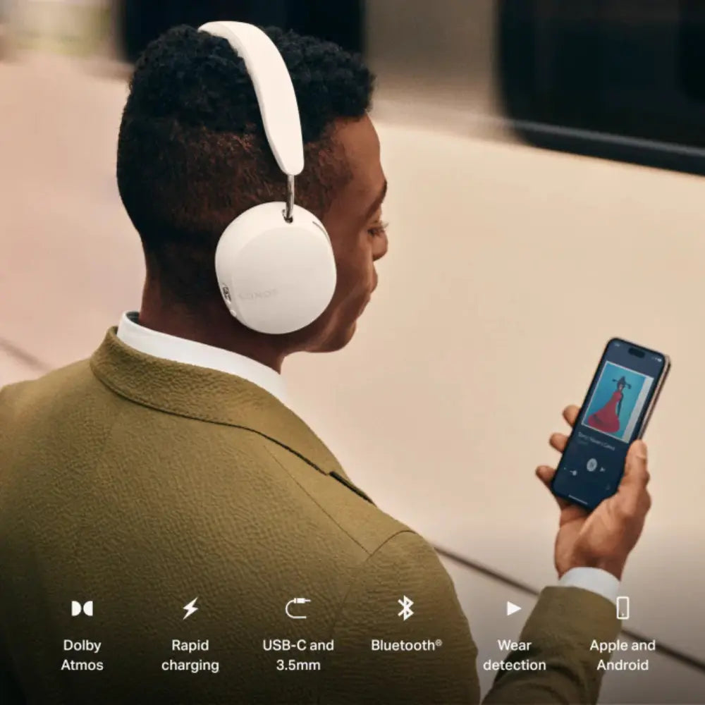 Person wearing white over-ear headphones; smartphone shows music app