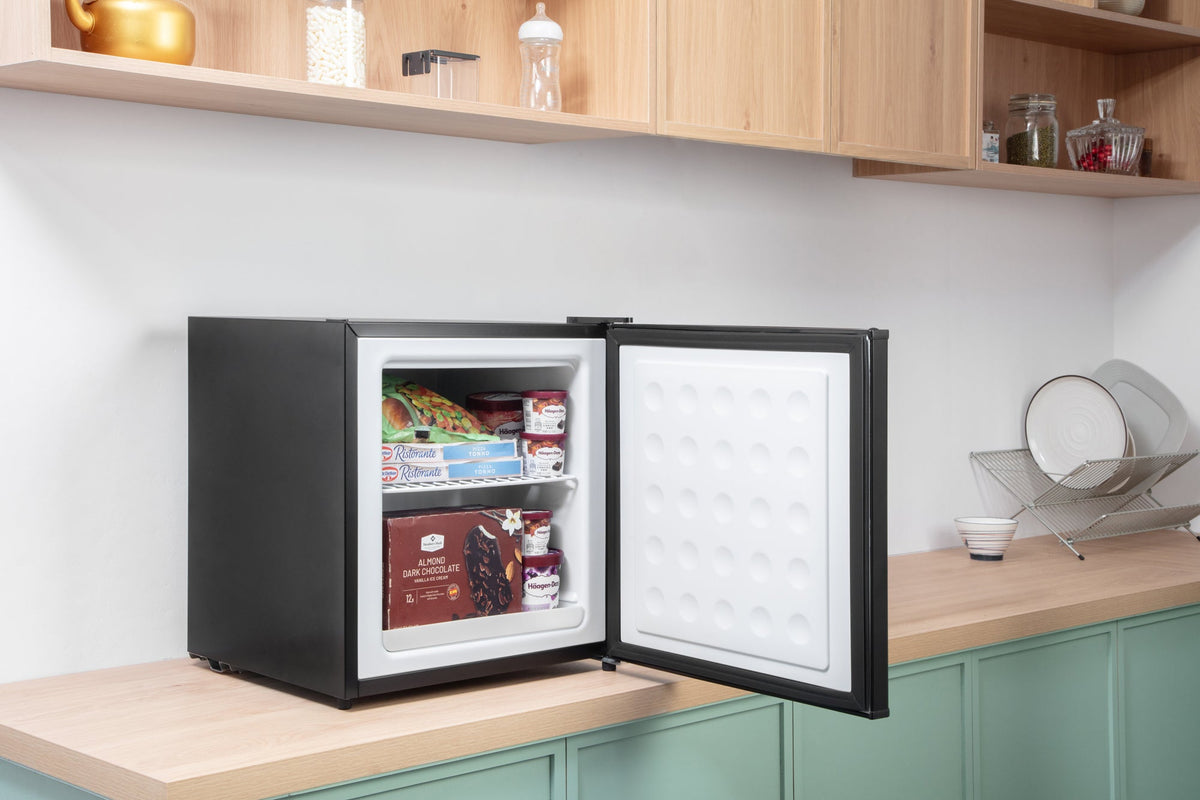 Black mini freezer with open door on a cabinet counter, stocked shelves inside