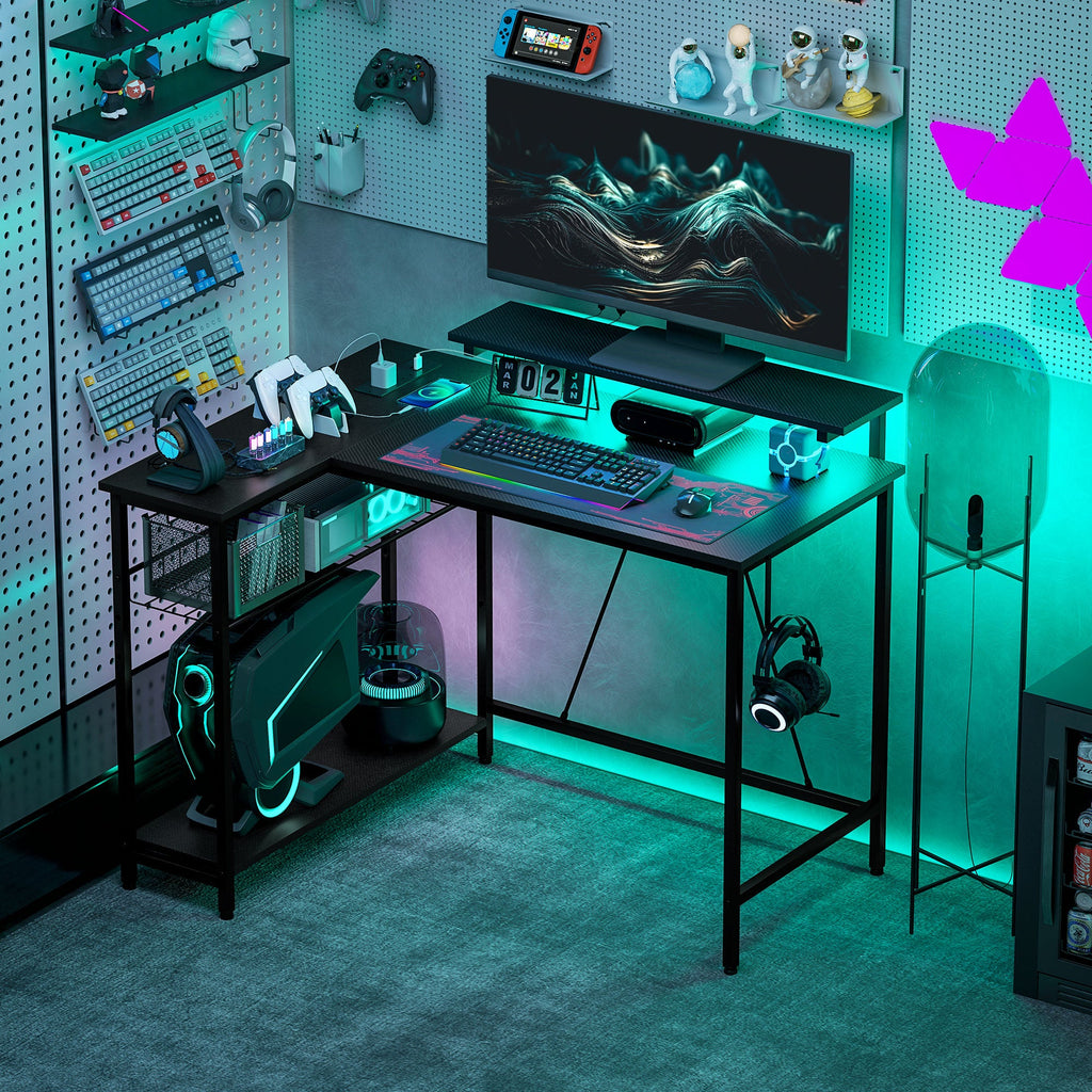 Black L-shaped gaming desk with monitor, keyboard, and vivid RGB LED accents.