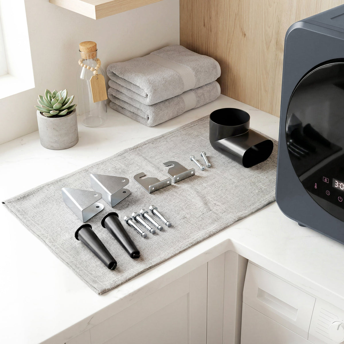 Grey front tumble dryer with included installation tools on a floor mat