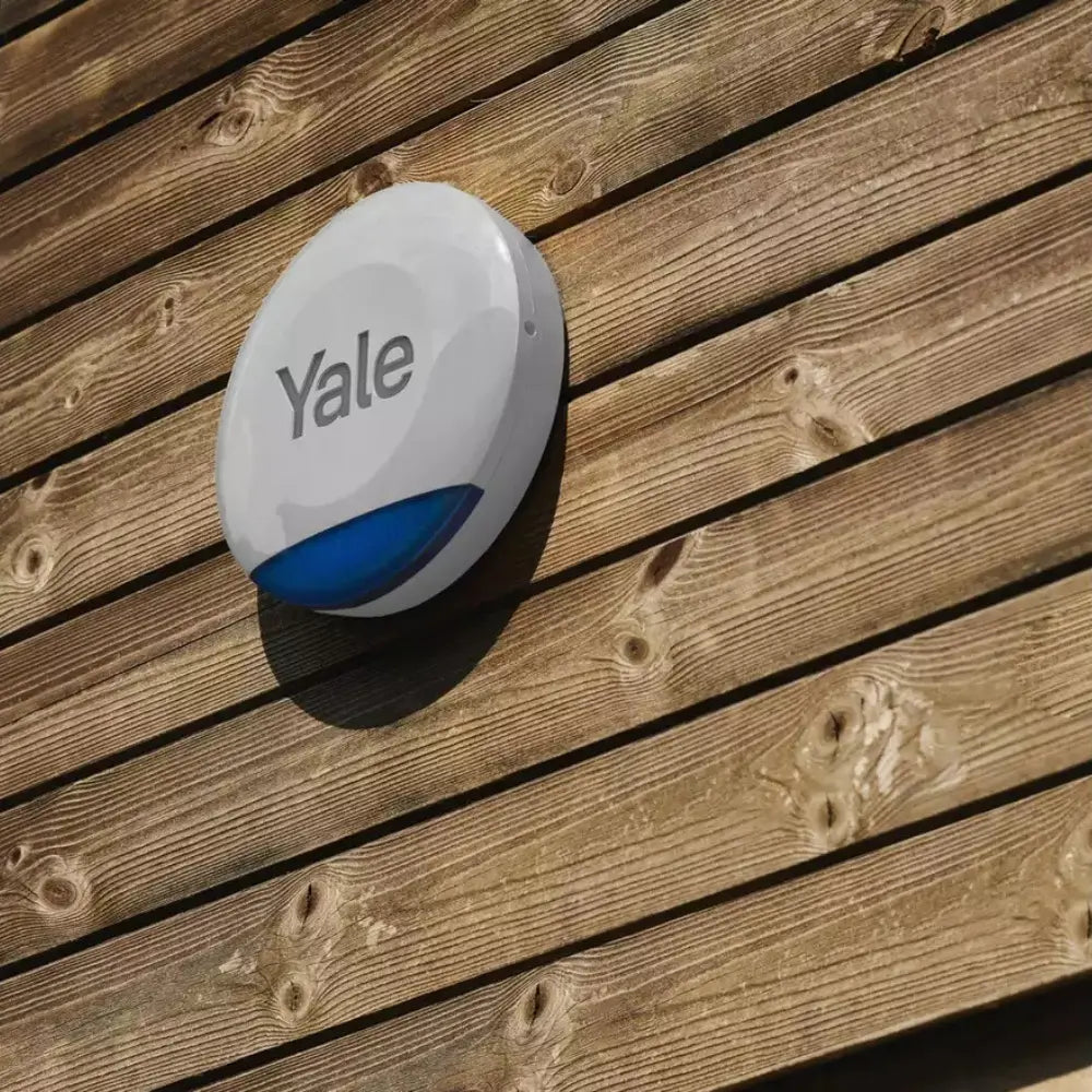 Grey YALE outdoor siren mounted on wooden fence with blue base