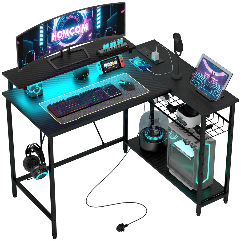Black L-shaped gaming/work desk with monitor, keyboard, and built-in RGB LED lighting.