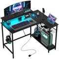 Black L-shaped gaming/work desk with monitor, keyboard, and built-in RGB LED lighting.