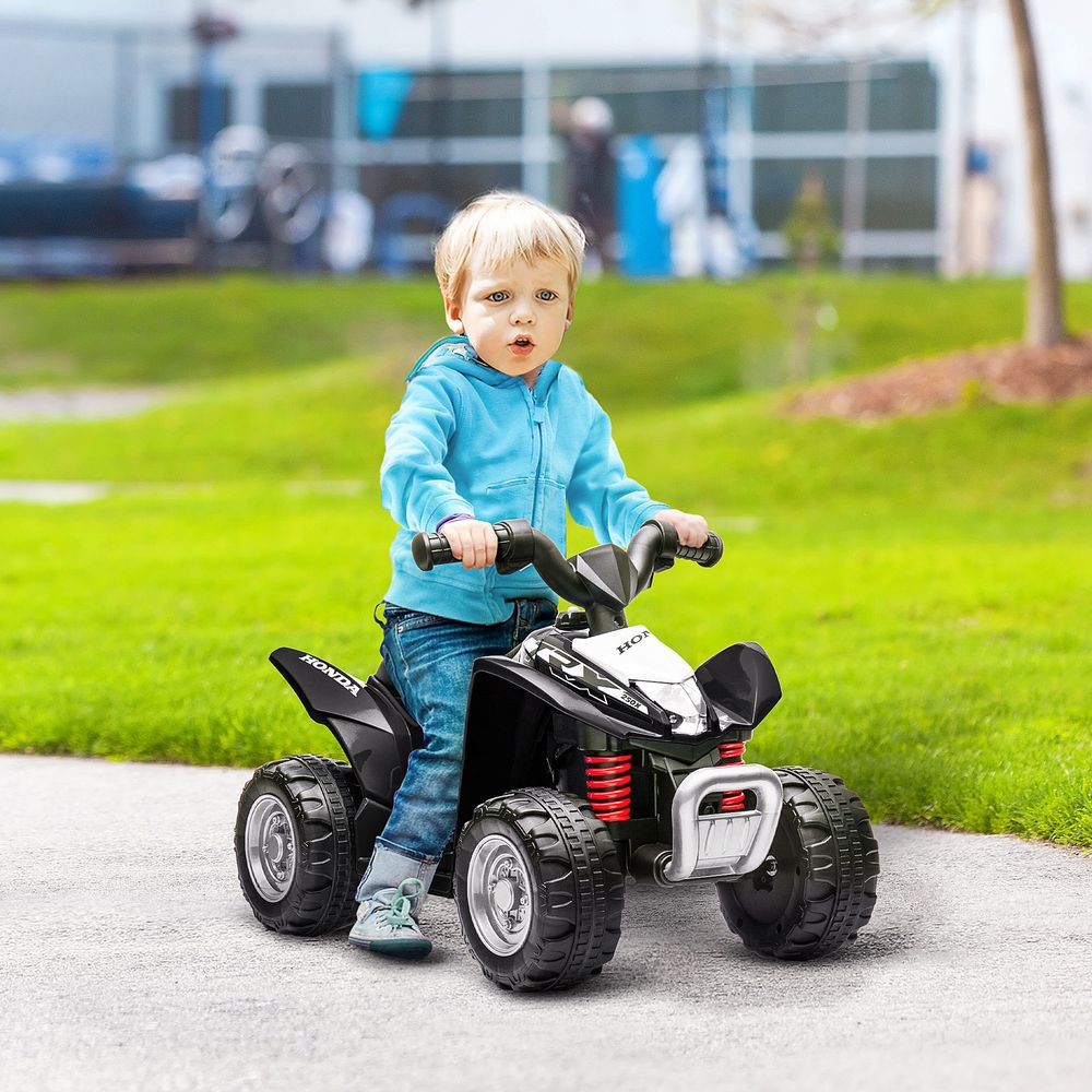 Black kids electric quad bike with child rider; thick tires and red rear suspension springs
