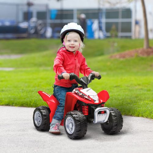 Red kids electric quad bike being ridden by a helmeted child on a paved path