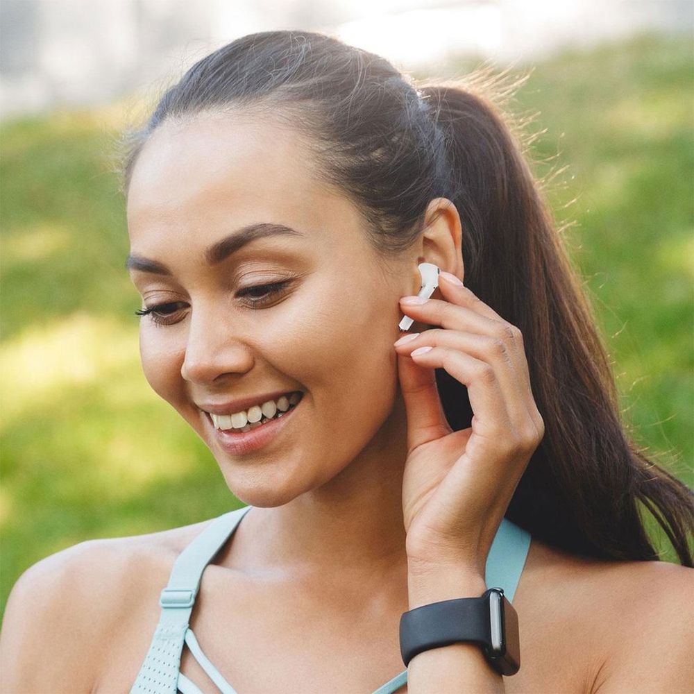 White wireless earbud worn in ear, speaker grille and microphone port visible