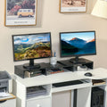 Black dual monitor stand riser with two elevated platforms on a desk, holding monitors