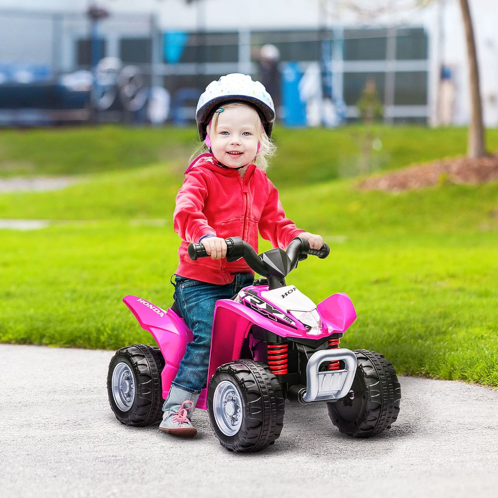 Kids riding pink electric quad bike with red suspension and front hand controls, outdoors