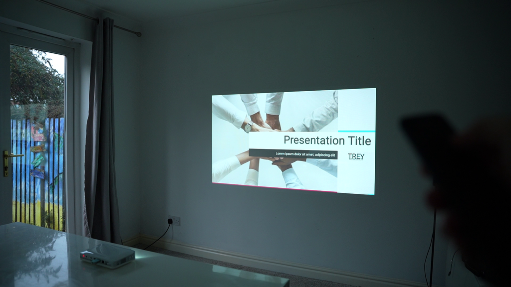 Ultra portable smart projector on a table, projecting a presentation on a screen